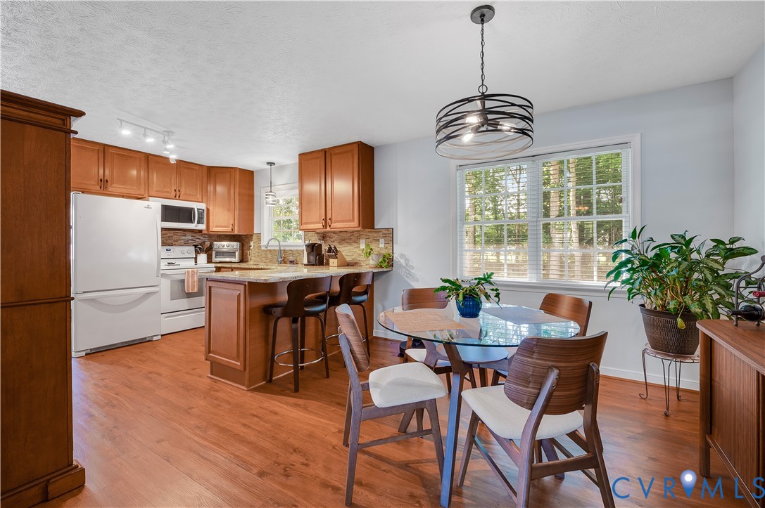 Kitchen and dining area featuring wood-finish flooring, wood cabinetry, granite countertops, and a window with natural light