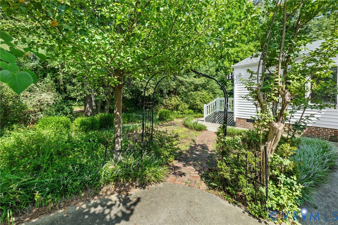 Lush landscaping with mature trees, a brick pathway, and a decorative metal archway
