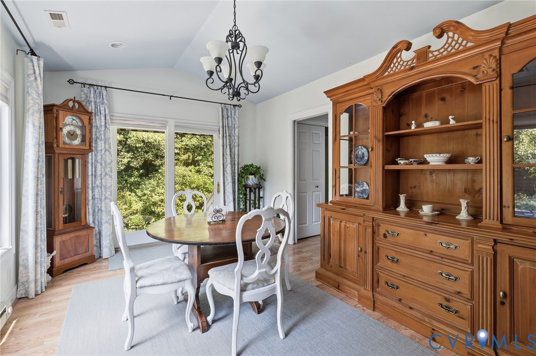 Vaulted ceiling, wood-finish flooring, sliding glass door, and elegant chandelier