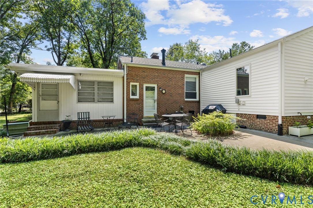 Brick and siding exterior with concrete patio, mature landscaping, and an awning over the entry