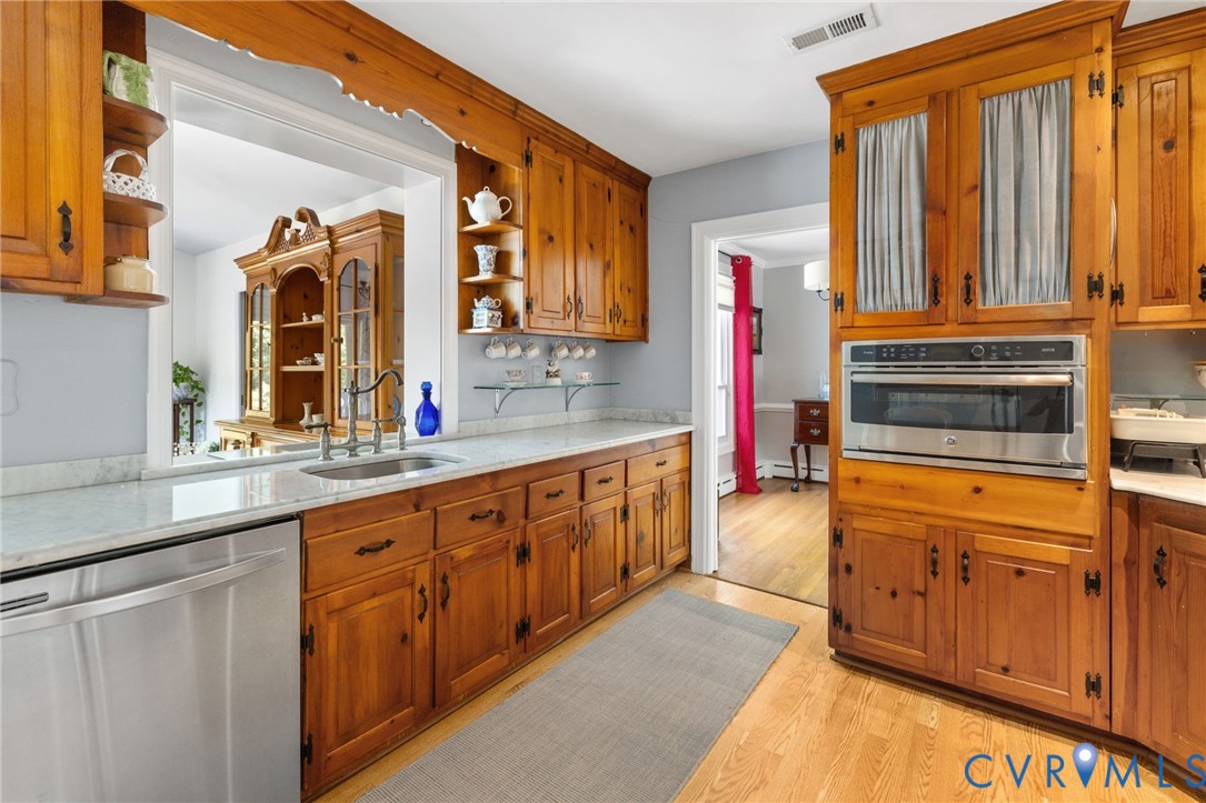 Wood cabinetry with dark hardware, undermount sink, stainless steel dishwasher, built-in microwave, and light-toned countertops Wood cabinetry with dark hardware, undermount sink, stainless steel dishwasher, built-in microwave, and light-toned countertops