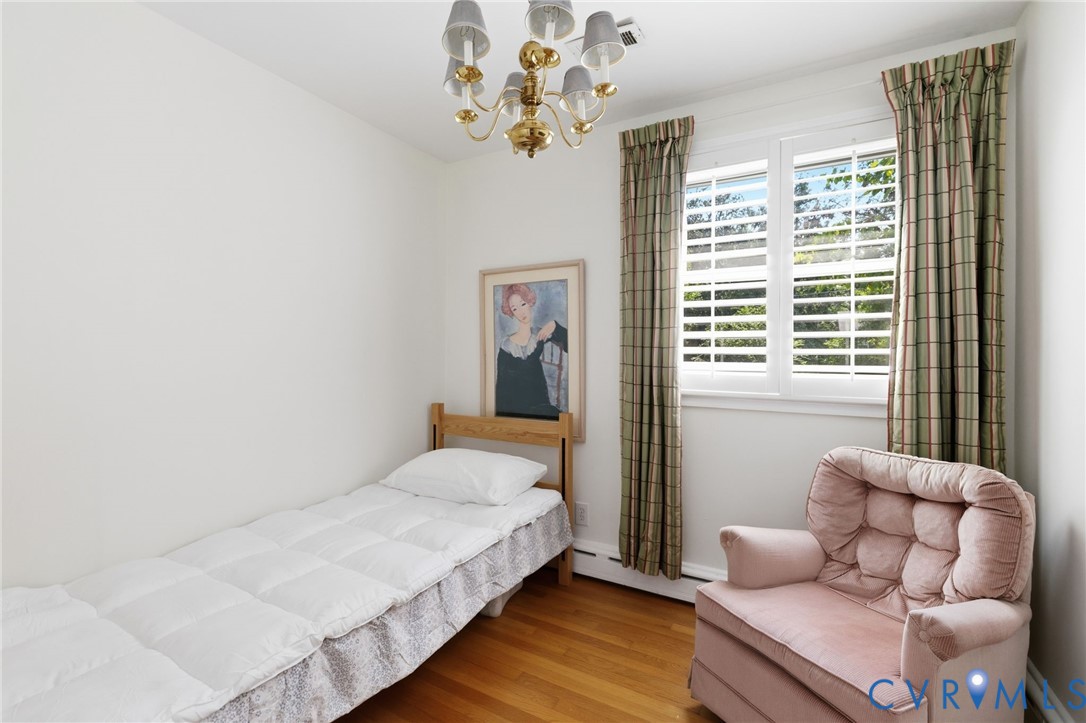 Hardwood flooring, white wall paint, window with plantation shutters, ceiling-mounted chandelier
