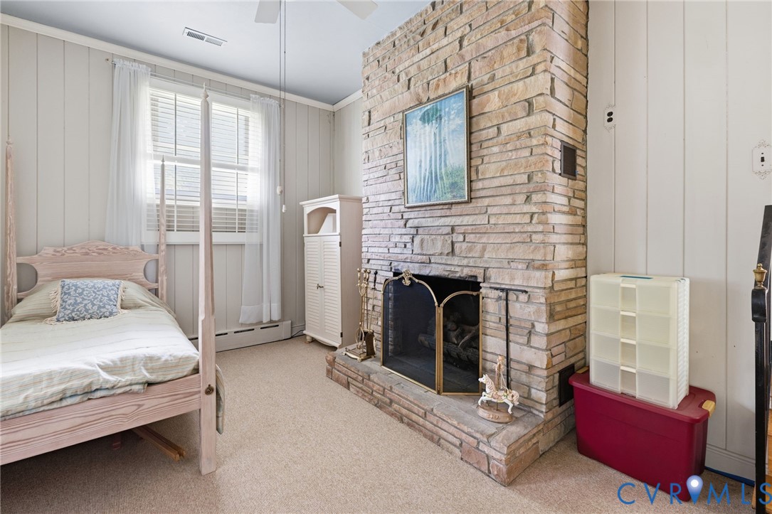 Stone fireplace with a black metal screen and hearth, light-colored wall paneling, and carpet flooring Stone fireplace with a black metal screen and hearth, light-colored wall paneling, and carpet flooring