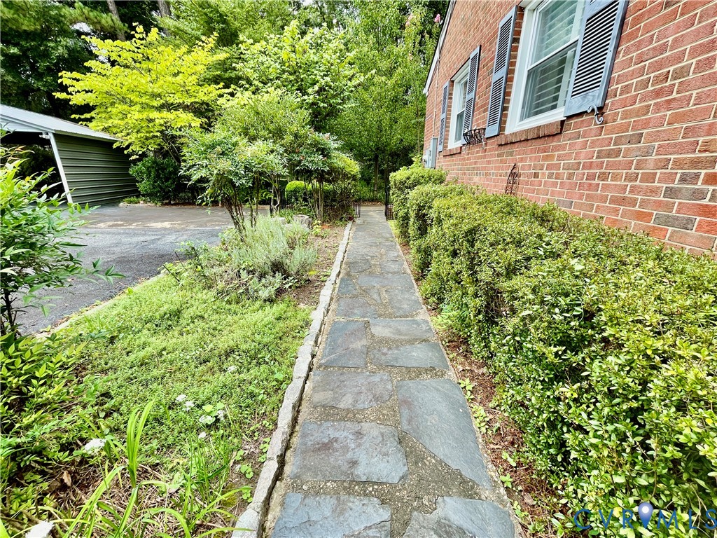 Brick exterior with window shutters, flagstone pathway, established shrubbery, and mature trees