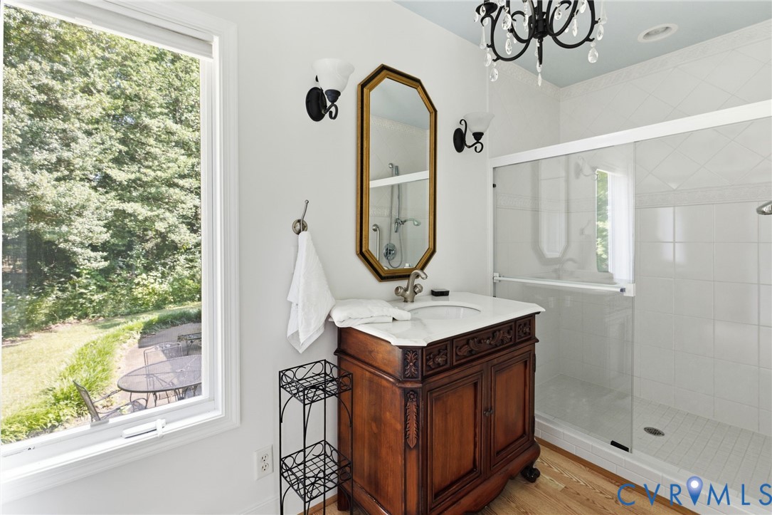 Bathroom featuring a carved wood vanity with a white countertop, a frameless glass shower enclosure, and a decorative chandelier