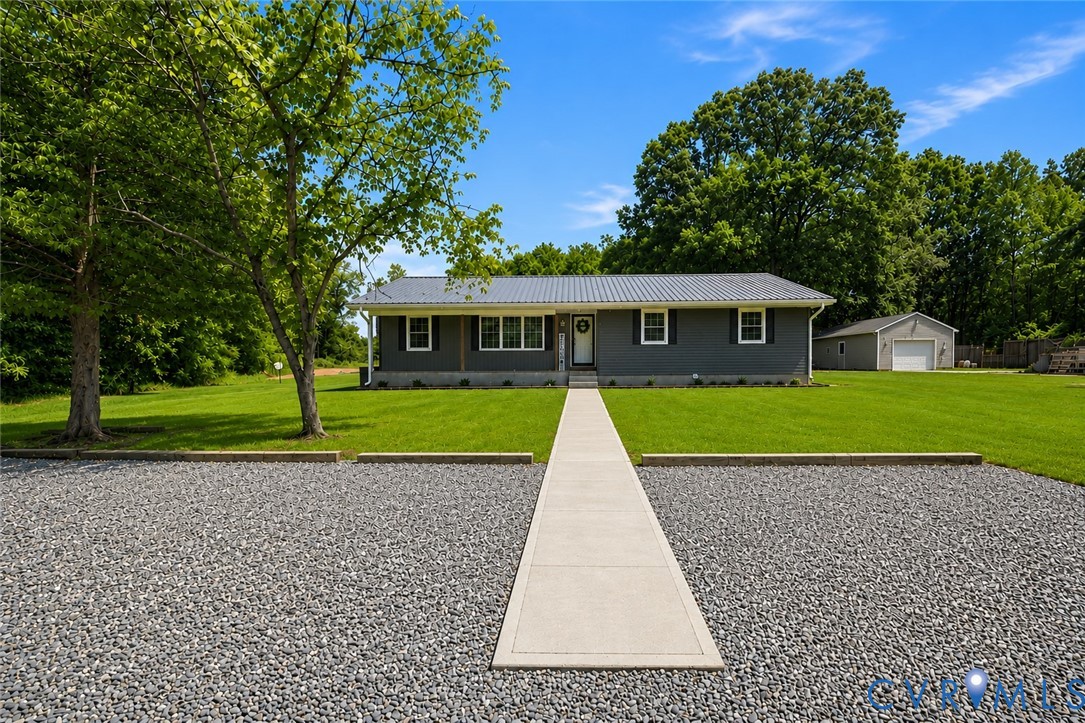 Welcoming ranch-style home set on expansive grounds featuring a straight concrete walkway approach, mature shade trees, and manicured lawn