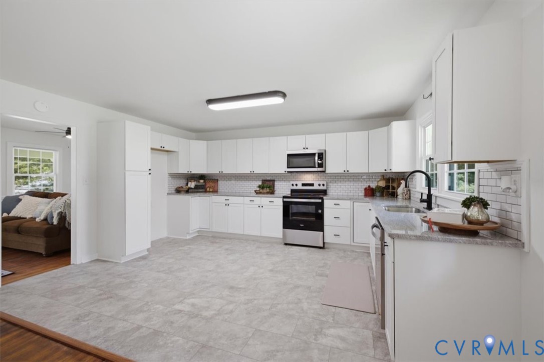 White cabinetry with black hardware, stainless steel appliances, light gray tile flooring, subway tile backsplash, and a black gooseneck faucet