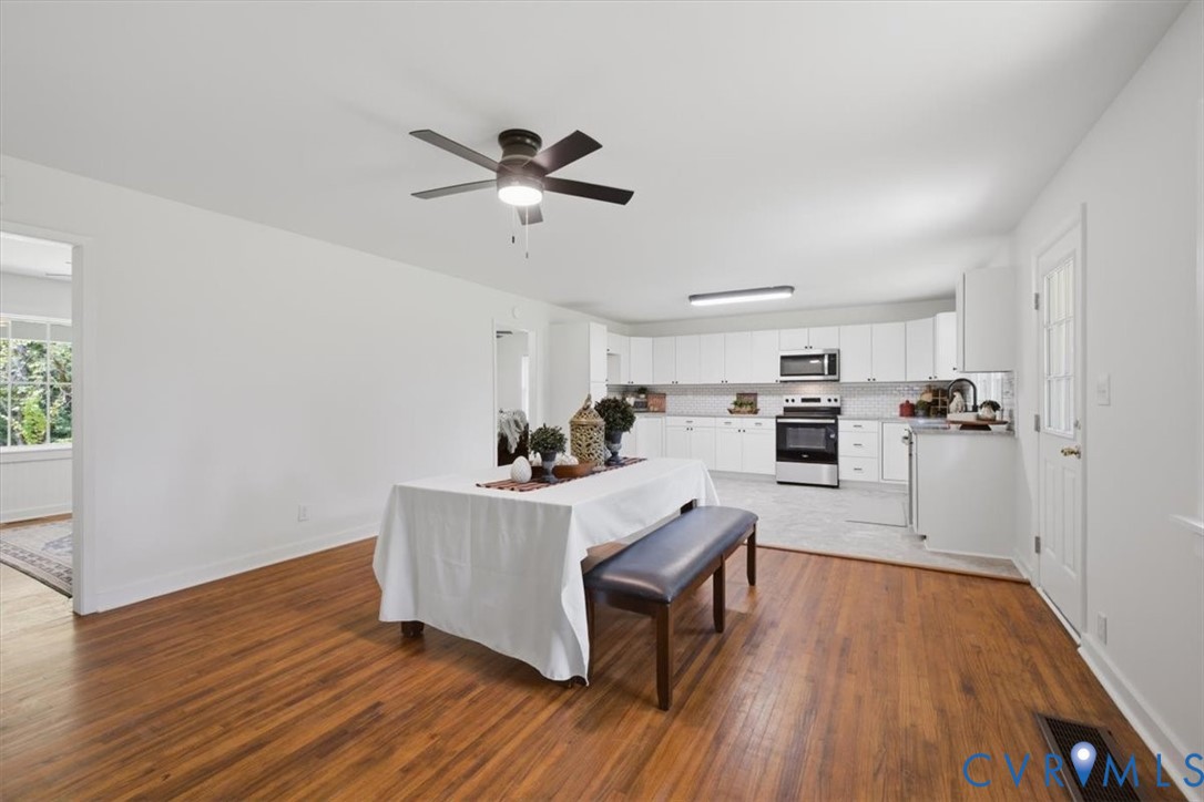 Hardwood flooring, ceiling fan with integrated lighting, white kitchen cabinetry, stainless steel appliances, and a tiled kitchen backsplash