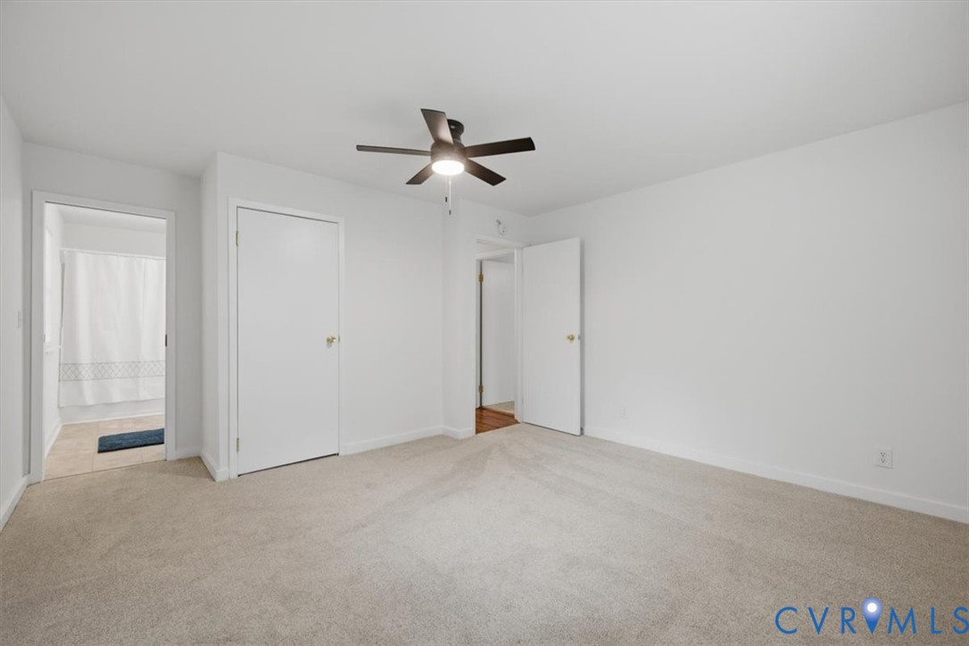 Neutral tone wall paint, light-colored carpet, ceiling fan with integrated lighting, white interior doors, and a bathroom with a shower/tub combination