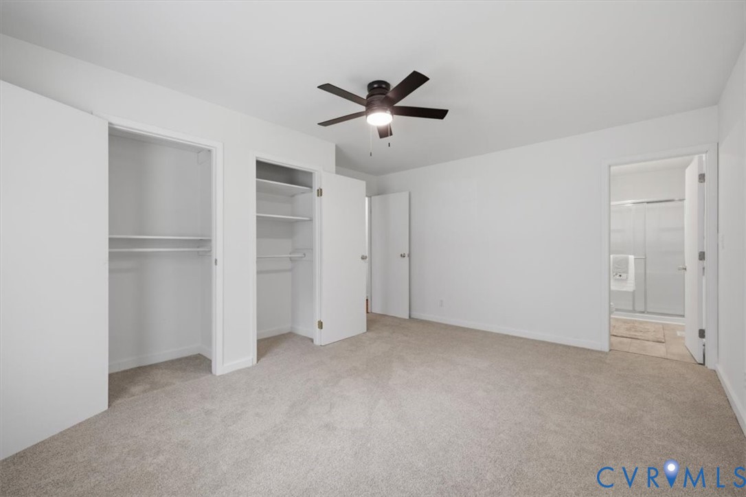 Carpeted room with a ceiling fan, two closet openings with shelving and hanging rods, and a doorway leading to a bathroom with a shower enclosure