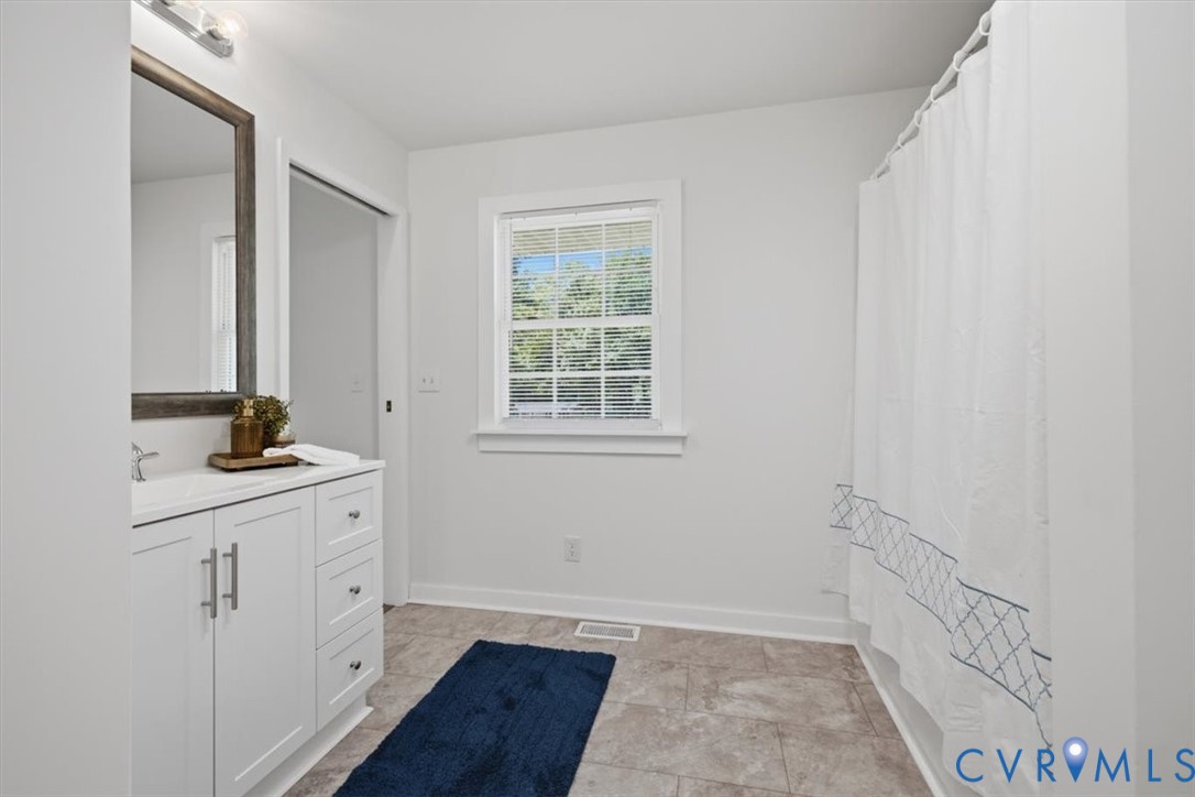 White vanity with a rectangular sink, wall-mounted mirror, and tile flooring