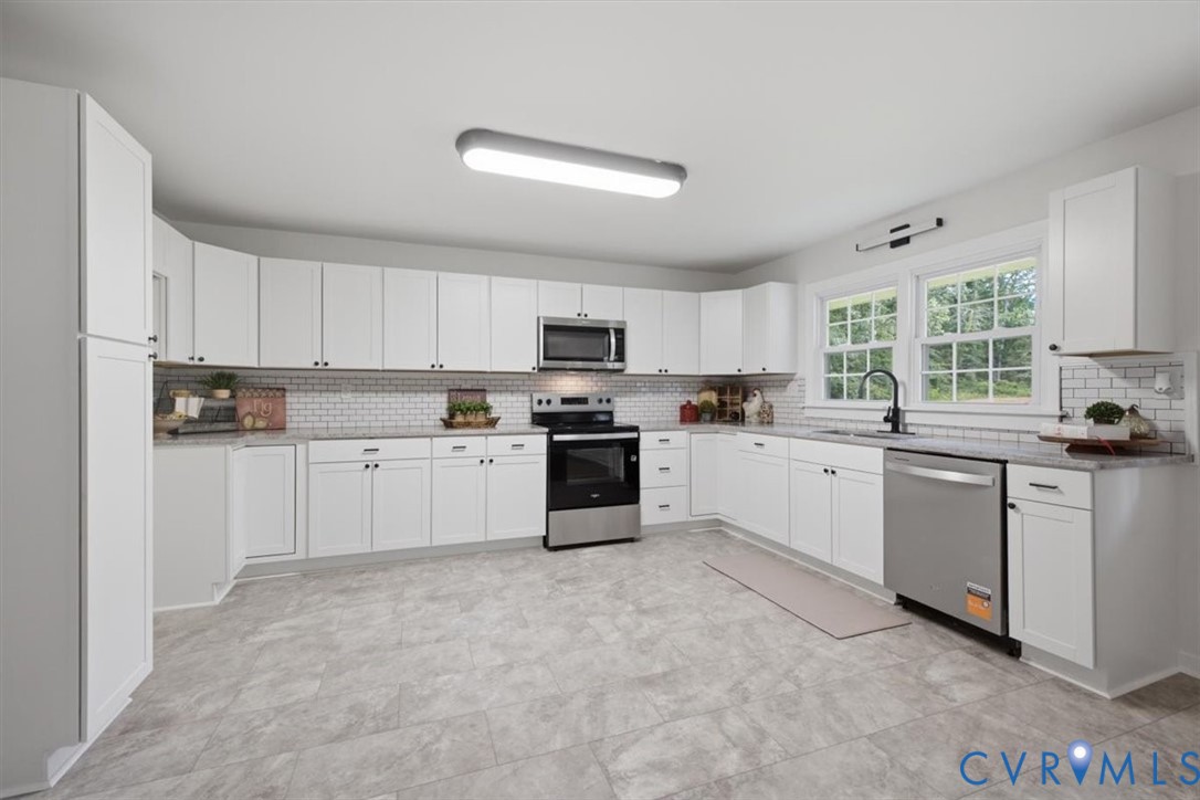 White shaker cabinetry with dark hardware, stainless steel appliances, grey countertop, subway tile backsplash, and light grey flooring