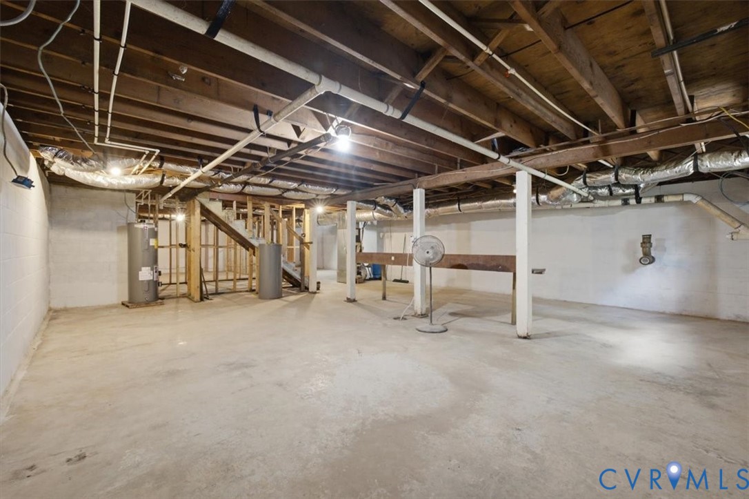 Unfinished basement featuring concrete flooring, exposed wood beam ceiling, support columns, and utility access