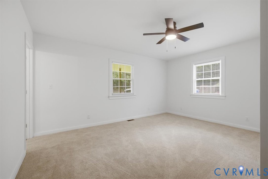 Neutral-toned carpet flooring, two windows with white trim, and a ceiling fan with integrated lighting