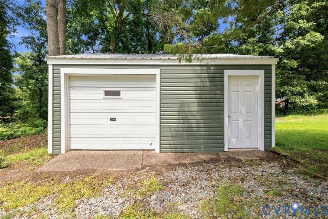 Detached auxiliary structure featuring horizontal siding, a single garage door with an integrated window, a side-entry door, and a metal roof