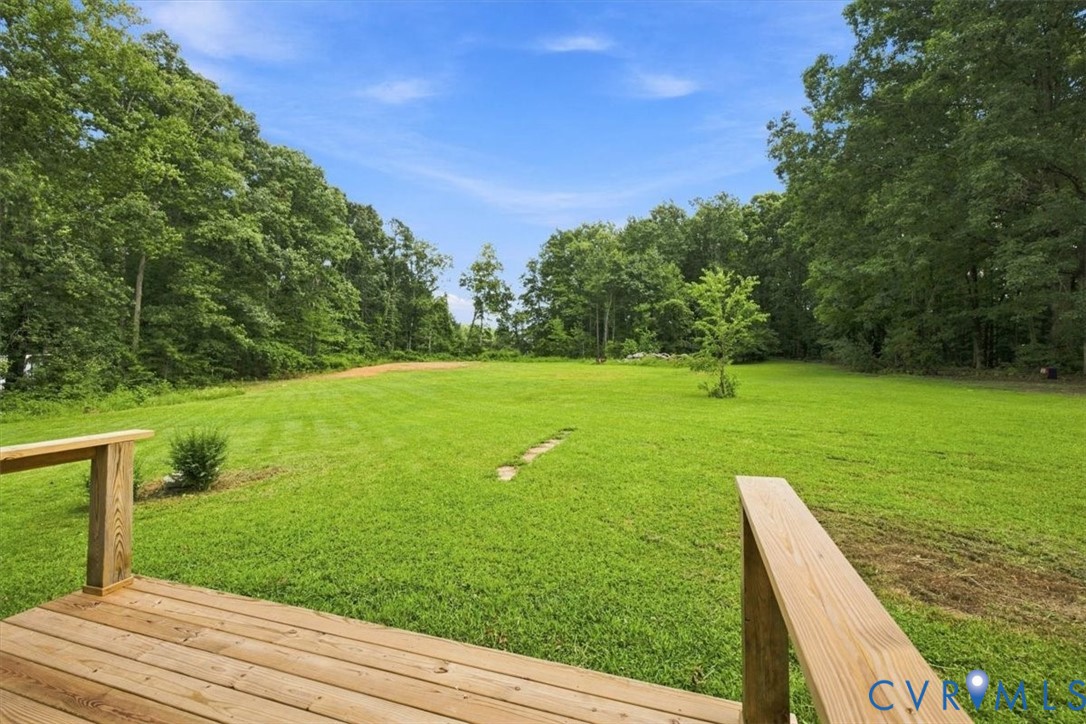 Expansive grassy lawn surrounded by mature trees, featuring a wooden deck with railing