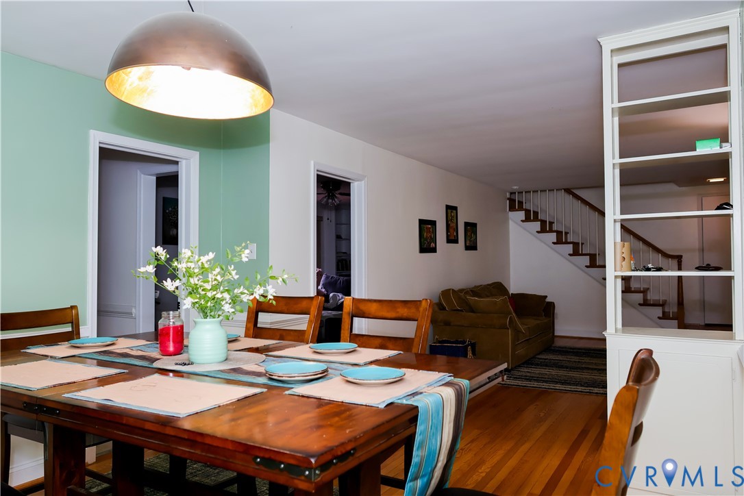 Hardwood flooring, open doorway leads to Kitchen, built-in shelving, and a prominent staircase Hardwood flooring, open doorway leads to Kitchen, built-in shelving, and a prominent staircase