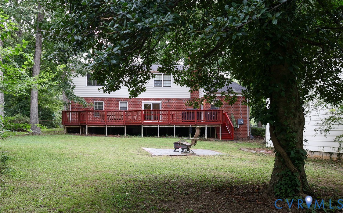 Expansive backyard featuring a large wood deck, brick and siding exterior, and mature trees