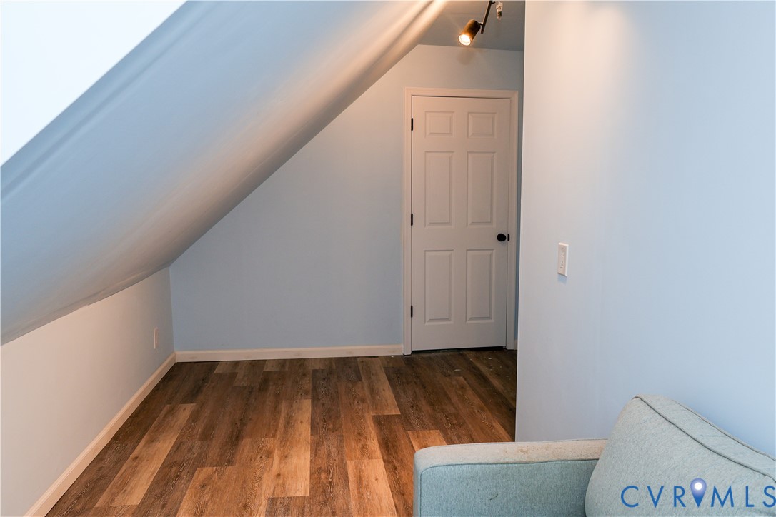 Sloped ceiling with, wood laminate-finish flooring, and a paneled interior door leading to storage area.