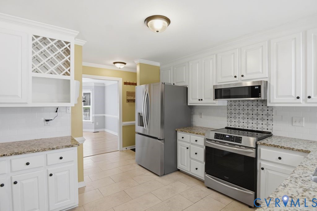 White shaker-style cabinetry with black hardware, granite countertops, stainless steel appliances, decorative tile backsplash, and neutral tile flooring
