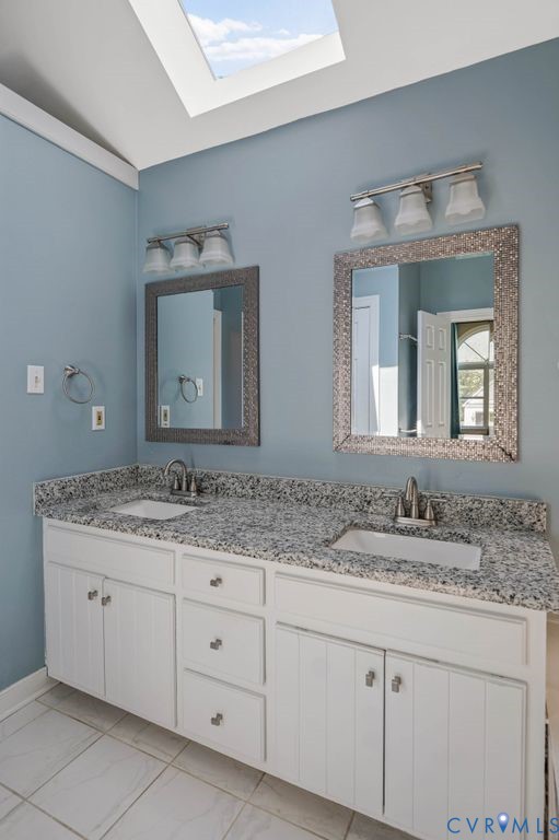 Dual vanity with integrated sinks, speckled countertop, white cabinetry, and a skylight
