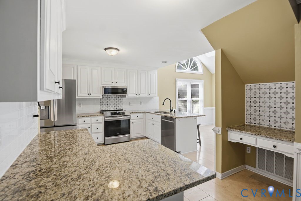 Kitchen featuring white cabinetry, granite countertops, stainless steel appliances, and a mosaic tile backsplash