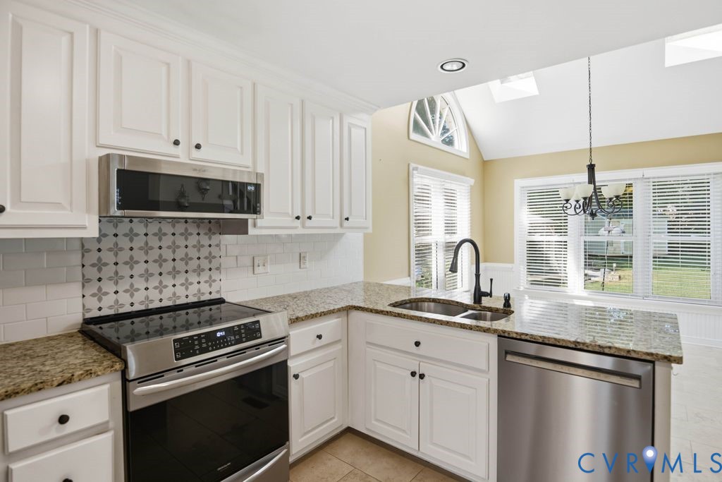 Kitchen featuring white cabinetry, granite countertops, stainless steel appliances, and a tile backsplash with decorative accents