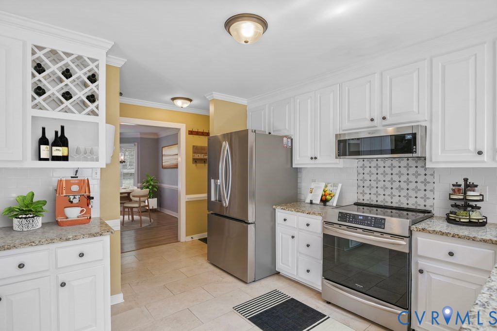 White cabinetry with dark hardware, stainless steel appliances, light-toned tile flooring, light-toned countertops, and a decorative tile backsplash