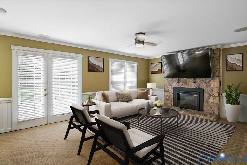 Stone-clad fireplace with black insert, double French doors, wood-finish ceiling fan, recessed lighting, and wall-mounted television