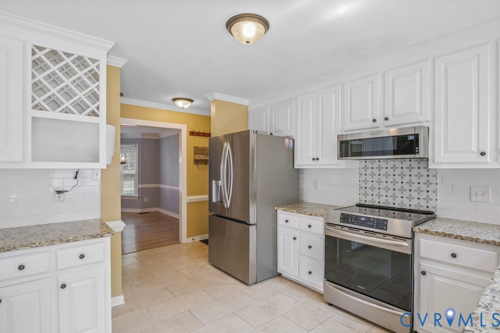 White cabinetry, granite countertops, tile flooring, built-in stainless steel microwave, and stainless steel range