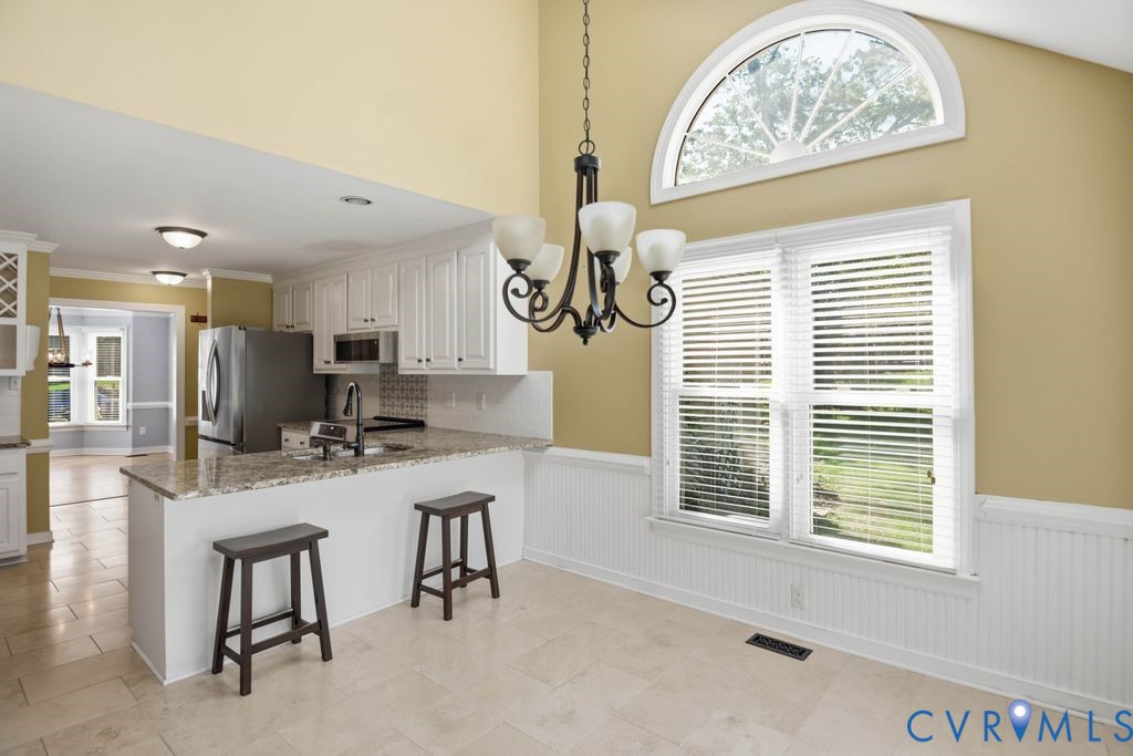 Vaulted ceiling with an arched transom window, a breakfast bar featuring a speckled countertop, tile flooring, and white wainscoting