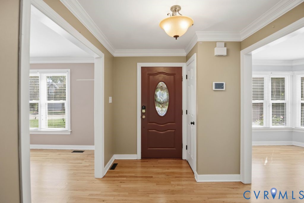 Hardwood flooring, crown molding, a decorative front entry door, and white window blinds