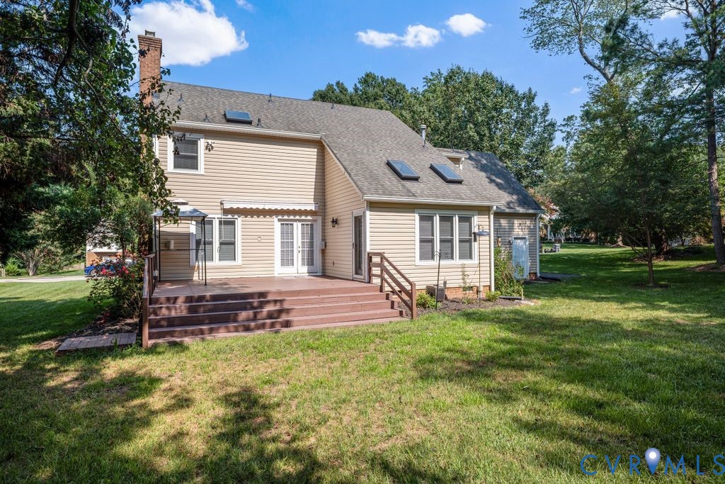 Expansive rear deck with integrated steps, dual French doors, beige siding, multiple skylights, and a brick chimney