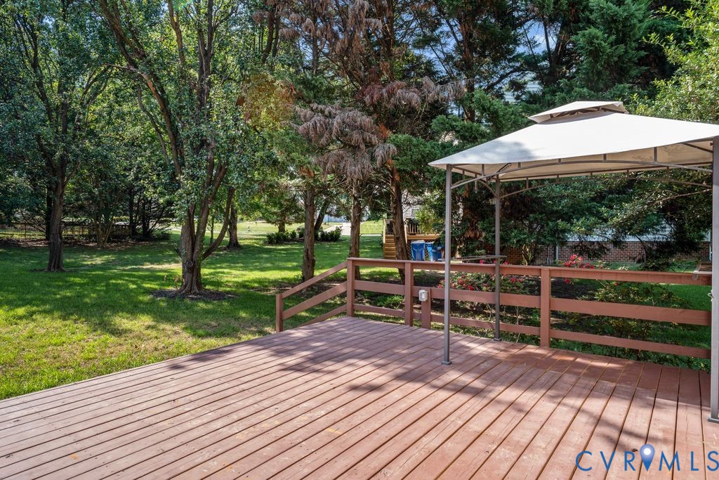 Expansive wood-finish deck with a perimeter railing, overlooking a lush green lawn and mature trees