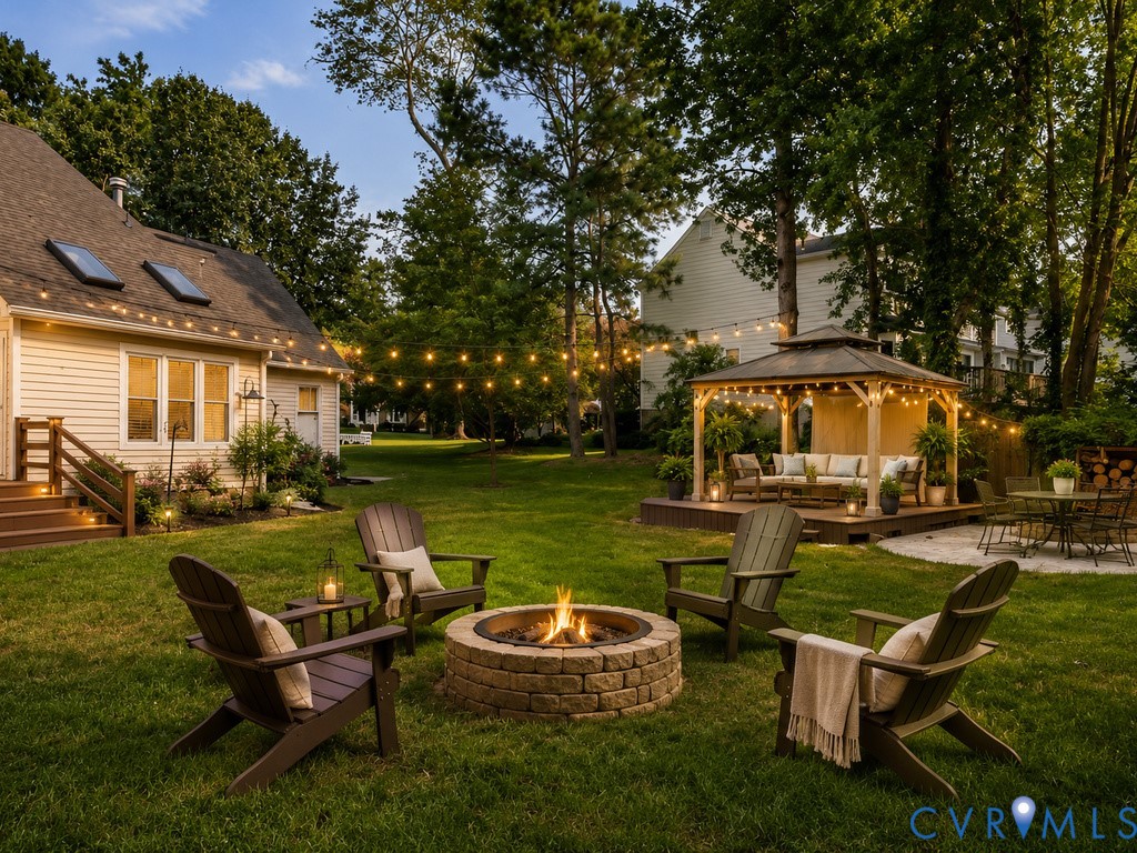 Expansive backyard oasis featuring a stone-constructed fire pit surrounded by mature landscaping, manicured lawn, and Adirondack seating