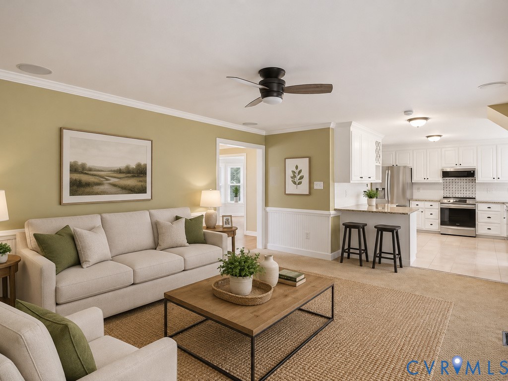 Open-concept living area with a ceiling fan, crown molding, and wainscoting