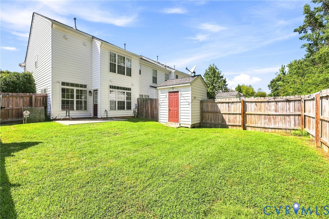 Expansive grassy yard with wood fencing, a storage shed, and a concrete patio Expansive grassy yard with wood fencing, a storage shed, and a concrete patio