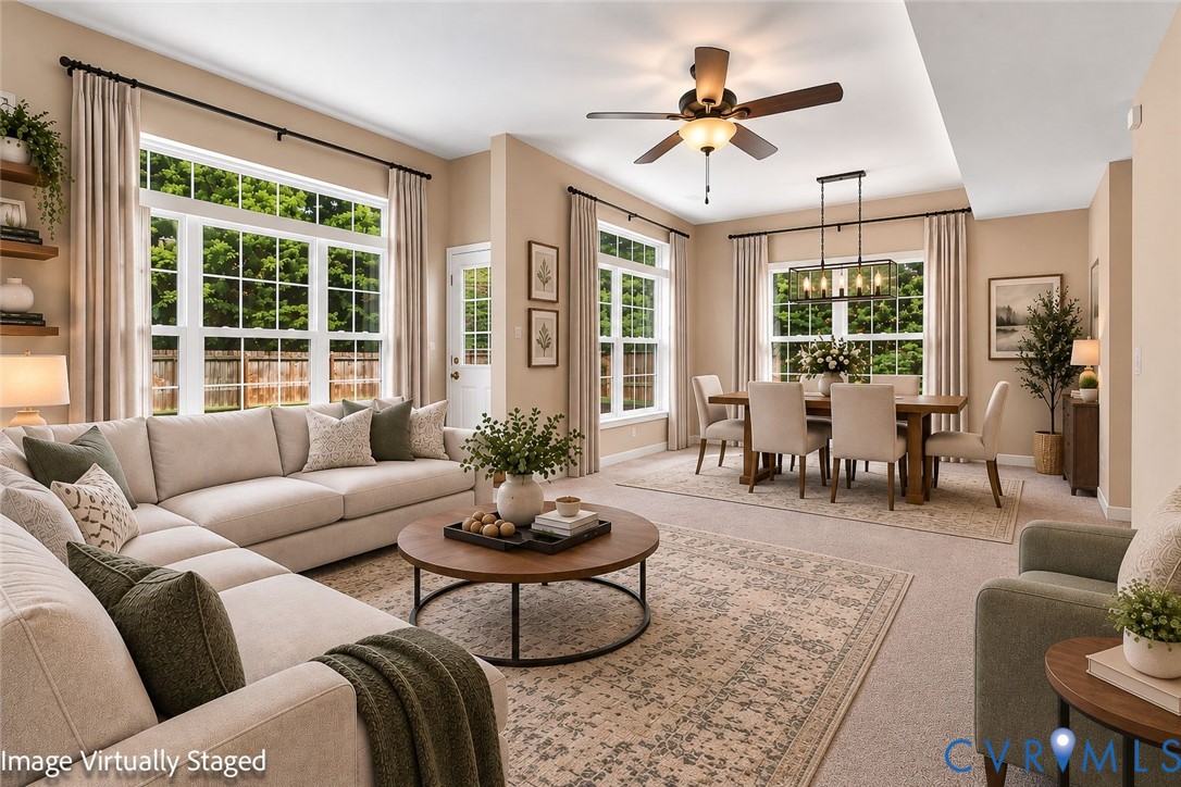 Open-concept living and dining area featuring a tray ceiling, multiple large windows, and a ceiling fan with integrated lighting