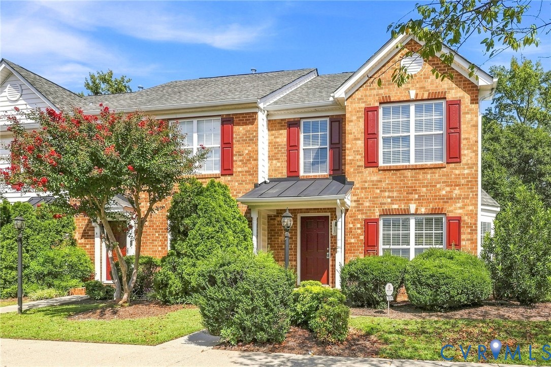 Brick exterior with red shutters, a prominent front door with an overhead awning, and established landscaping Brick exterior with red shutters, a prominent front door with an overhead awning, and established landscaping