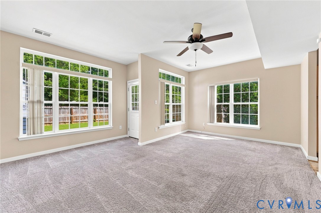 Plush carpet flooring, multiple windows with white trim, and a ceiling fan with integrated lighting
