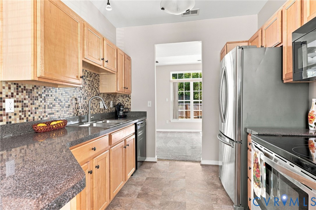 Kitchen featuring wood cabinetry, stainless steel appliances, mosaic tile backsplash, and stone-finish countertops