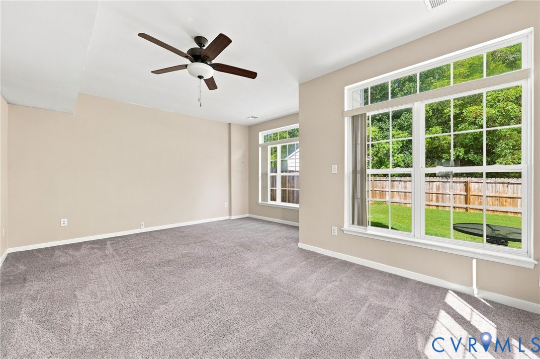 Neutral-toned walls, high ceilings, ceiling fan, large windows, and gray carpeted flooring