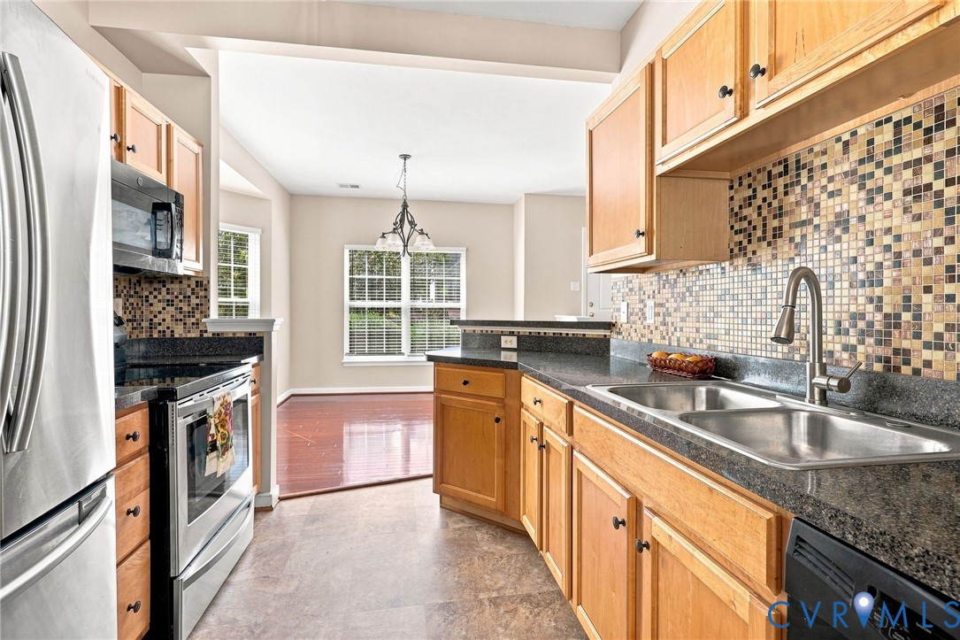 Kitchen featuring wood cabinetry, dark countertops, a mosaic tile backsplash, a double stainless steel sink, and stainless steel appliances