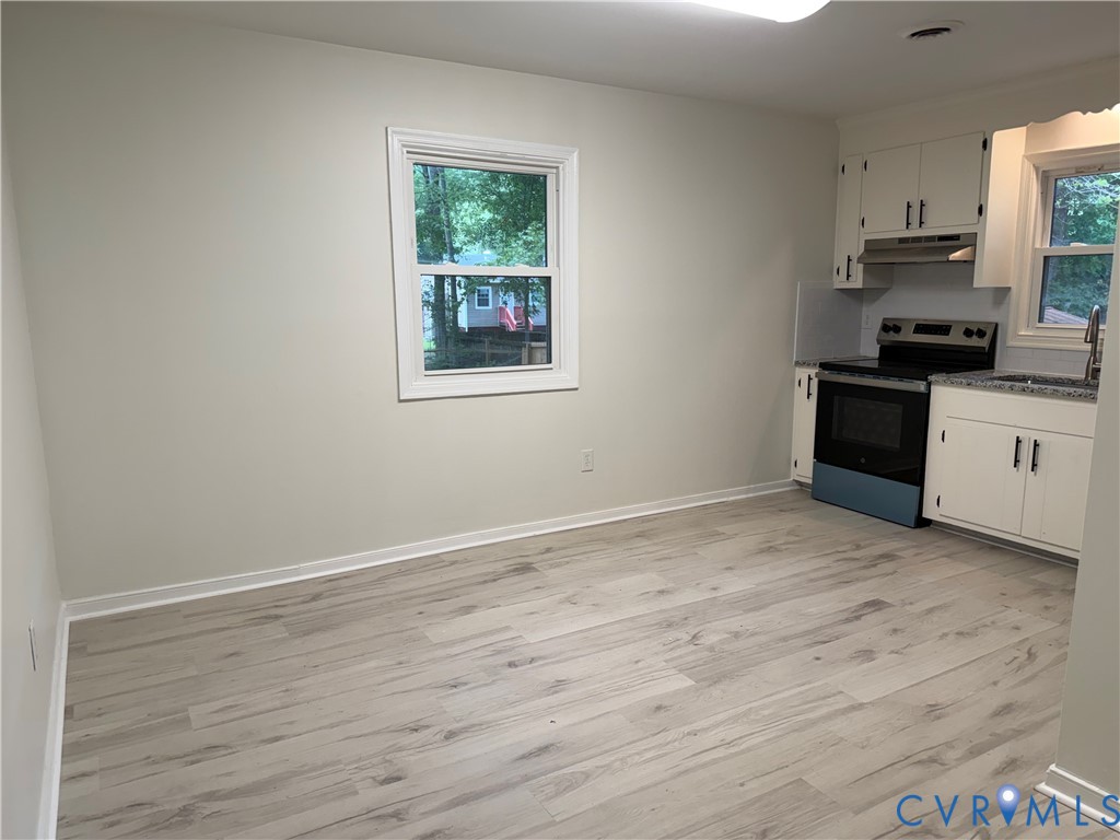 Kitchen area featuring white cabinetry, stainless steel range with overhead microwave, granite-style countertops, and wood-finish flooring