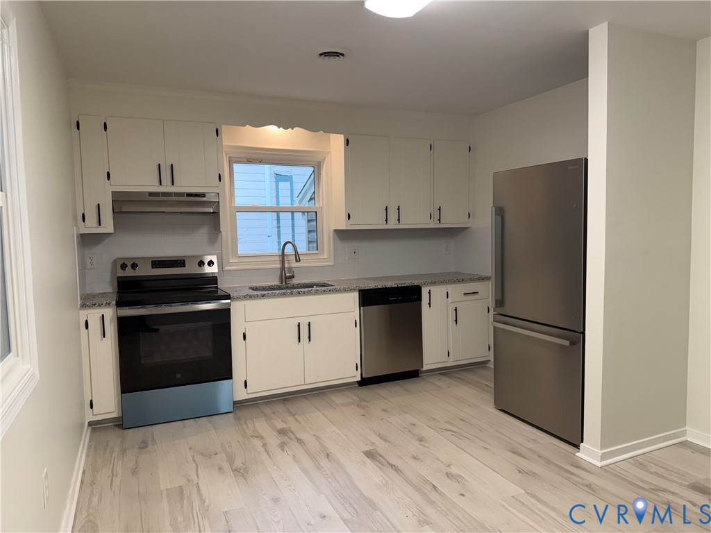 White cabinetry with black hardware, stainless steel appliances, light-toned wood-finish flooring, and light-toned countertops