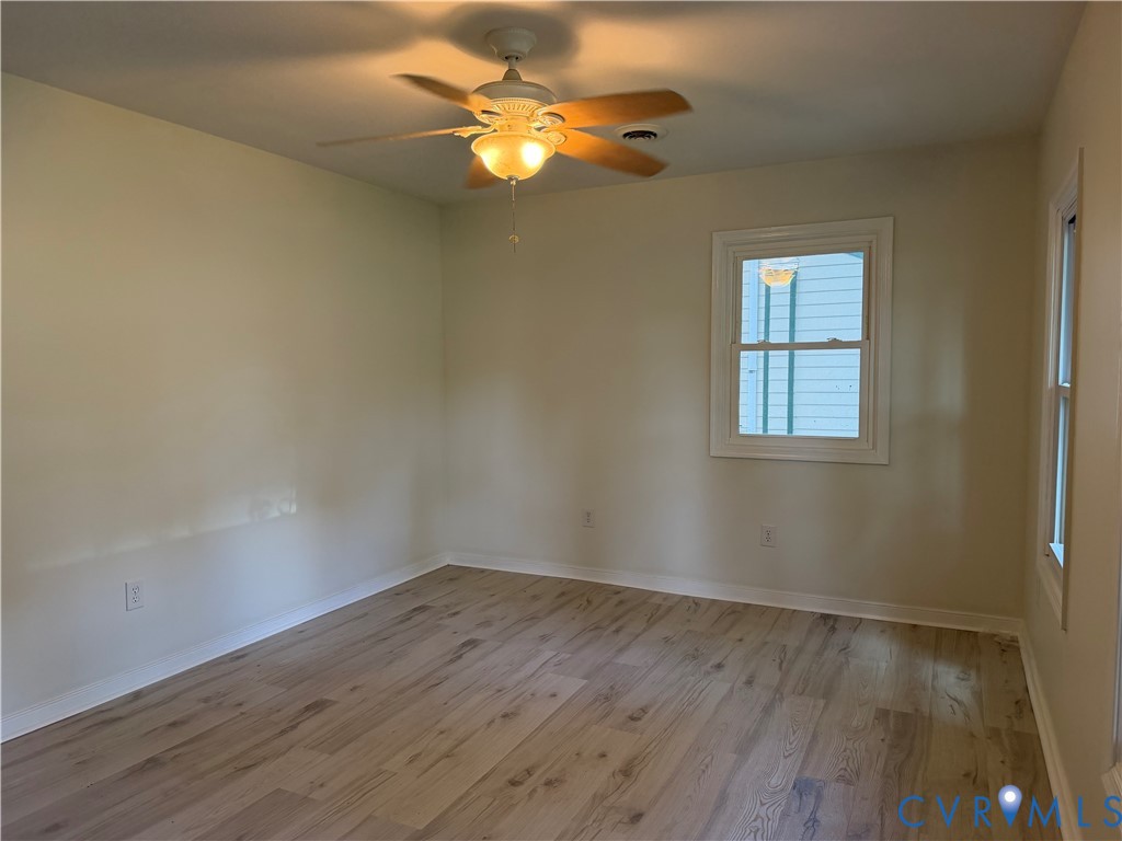 Light-toned wood-finish flooring, two windows with white trim, and a ceiling fan with integrated lighting