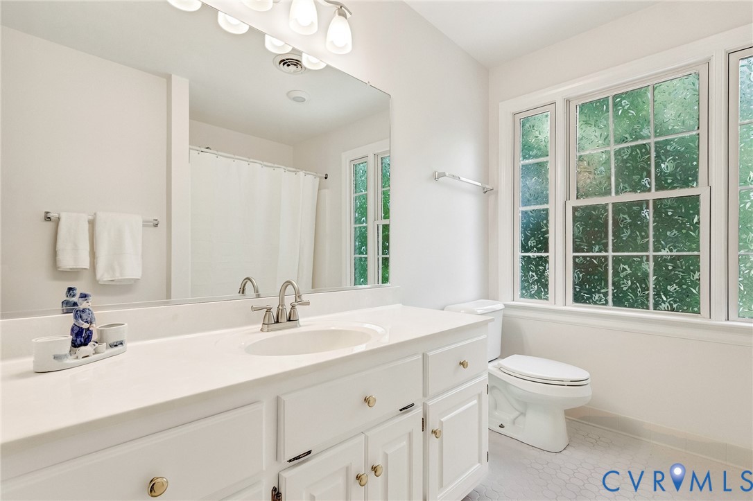 Vanity with a single basin sink, white cabinetry with brass hardware, and a large wall-mounted mirror