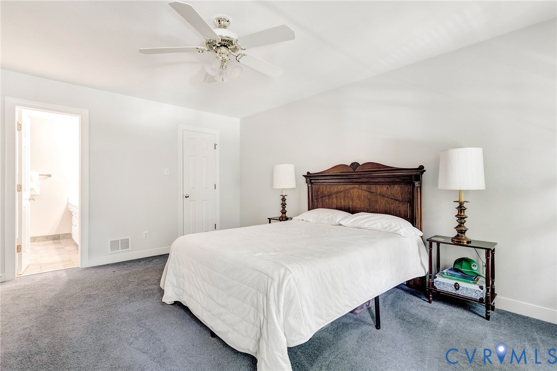 Spacious primary bedroom featuring a wood-finish headboard, ceiling fan with integrated lighting, neutral wall finishes, and carpeted flooring