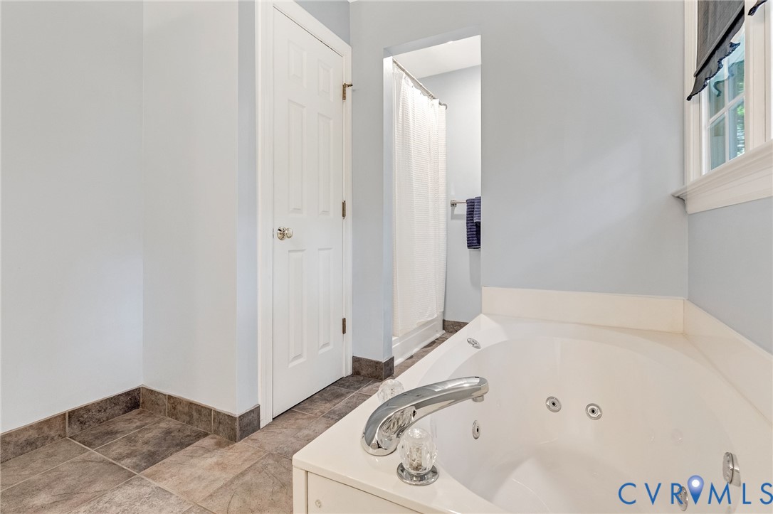 Corner jetted soaking tub with chrome fixtures, tiled flooring, and a separate shower enclosure