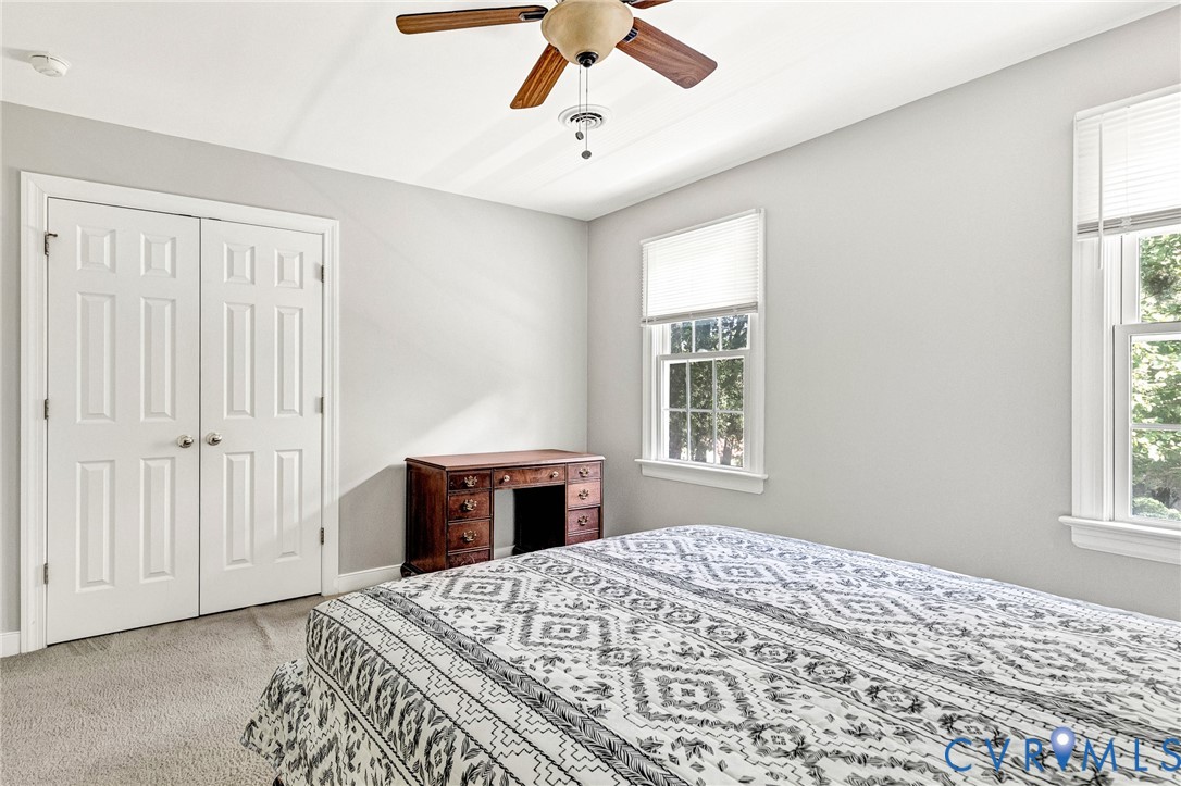 Carpeted flooring, white six-panel bifold doors, window with white blinds, white trim, and a ceiling fan with light fixture